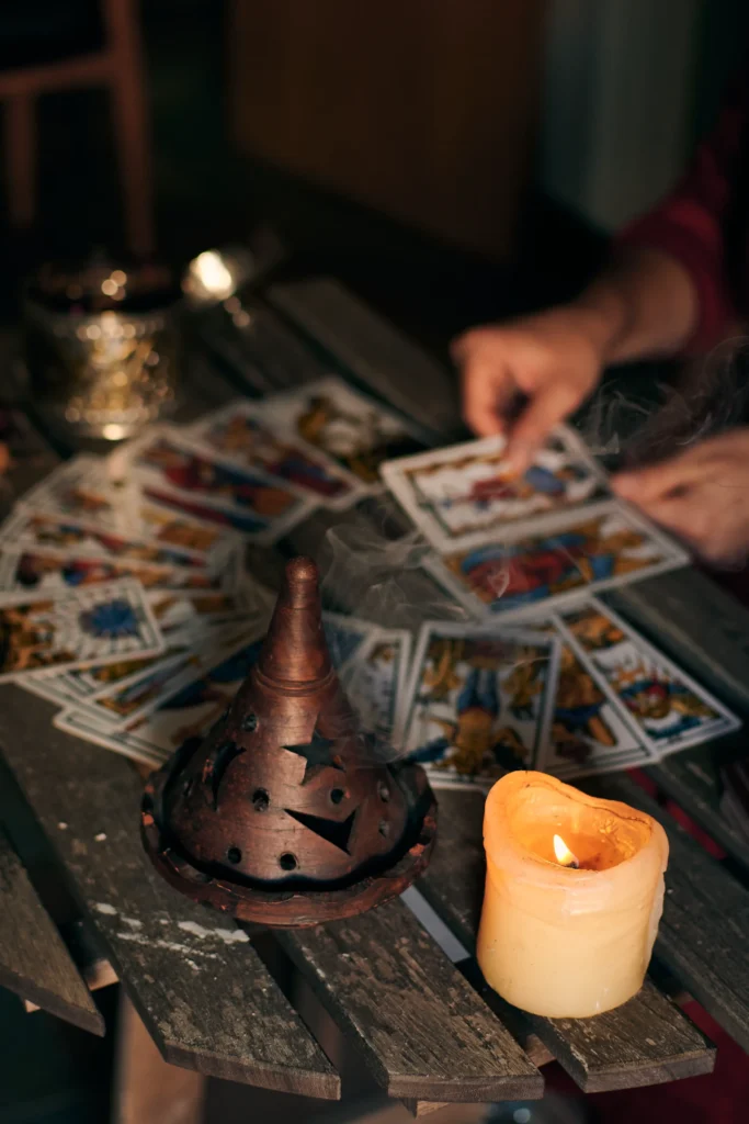 A wooden table scattered with tarot cards, a burning candle, and an incense burner emitting smoke, creating a mystical atmosphere.